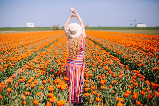 Woman with long red hair wearing a striped dress  standing by the back on colorful tulip field.