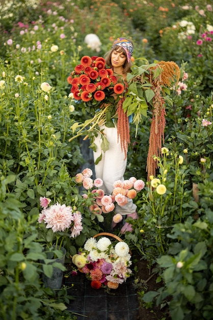 屋外のダリア農場にたくさんの花を持つ女性