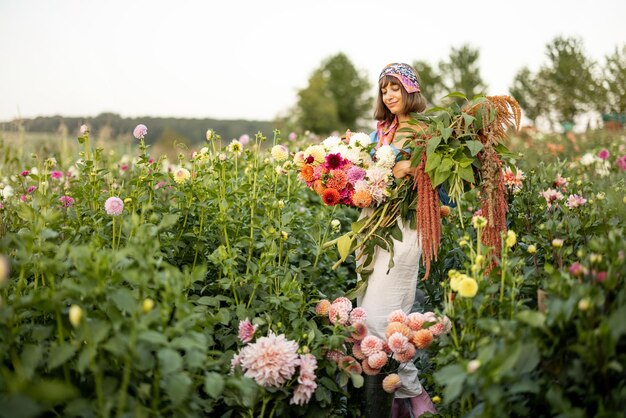 屋外のダリア農場にたくさんの花を持つ女性