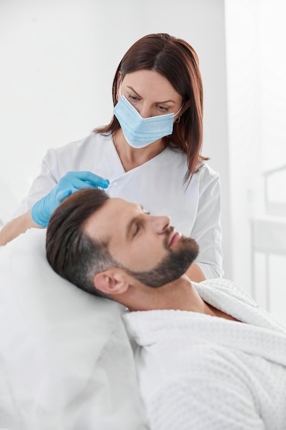 Woman with mask does vitamin injection in patient head skin during antiaging meso therapy