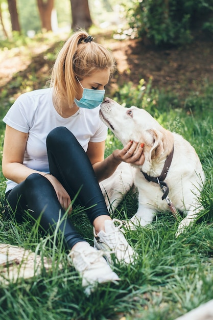 マスクを持つ女性は彼女の犬と一緒に外で時間を楽しんでいます