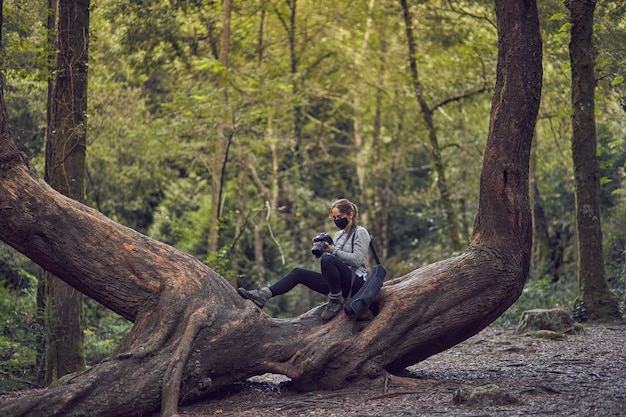 woman with mask taking photos on a tree trunk