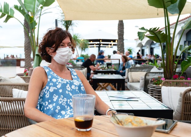 woman with mask at terrace having a soda