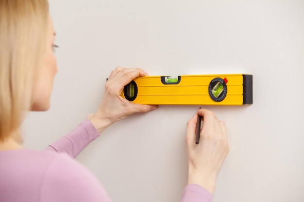 Woman with measuring tape. Rear view of blond hair woman taking measurements of the wall