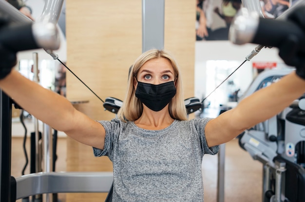 Donna con maschera medica e guanti allenamento in palestra