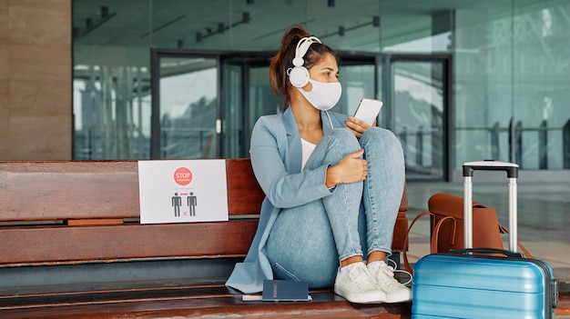 Foto donna con mascherina medica e cuffie e l'aeroporto durante la pandemia