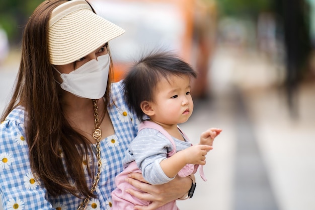 Woman with medical mask to protect coronaviruscovid19 while holding baby in the city