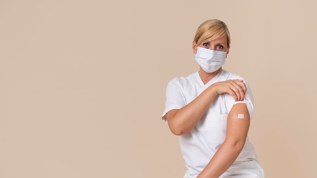 Woman with medical mask showing arm with sticker after getting a vaccine