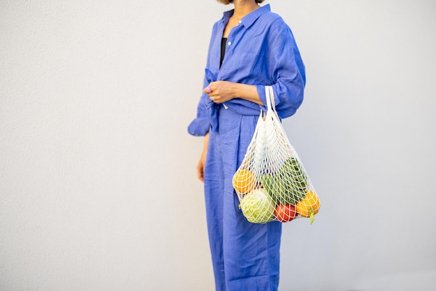 Woman with mesh bag full of fresh fruits outdoors