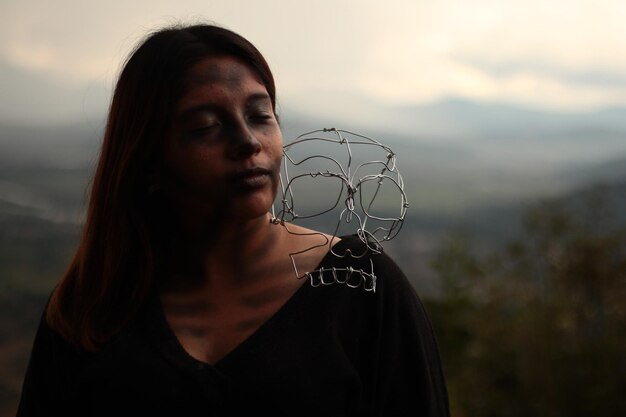 Foto donna con un teschio di metallo sulla spalla mentre si trova all'aperto durante il tramonto