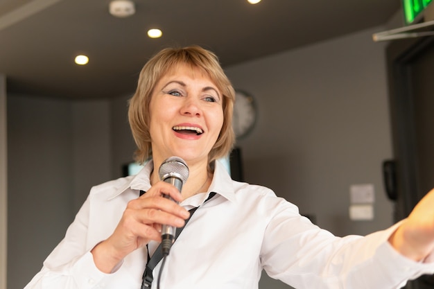 Foto una donna con un microfono nella sala davanti al pubblico durante una conferenza e una presentazione. donna di mezza età davanti agli elettori.