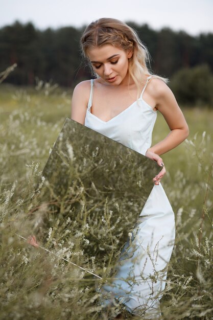 Woman with mirror in hand in the field at sunset