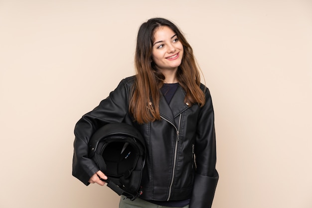 Woman with a motorcycle helmet on beige wall laughing and looking up