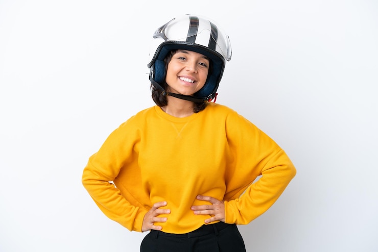 Photo ヒップで腕と笑顔でポーズをとってオートバイのヘルメットを持つ女性