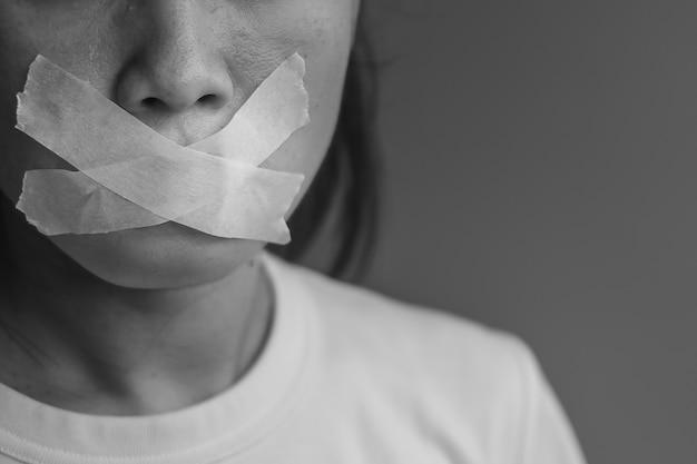 woman with mouth sealed in adhesive tape. free of speech, freedom of press, human rights, protest dictatorship, democracy, liberty, equality and fraternity concepts
