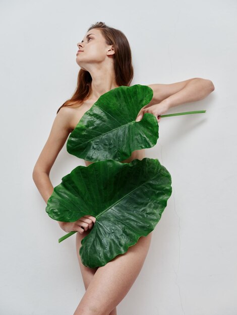 Woman with naked body and green leaves light background