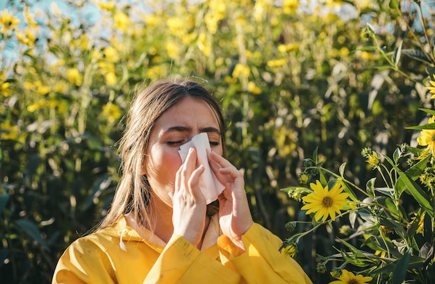 Woman with napkin fighting blossom allergie outdoor Portrait of an allergic girl surrounded by seasonal flowers in bright yellow color Beautiful girl having an allergic reaction to flowers