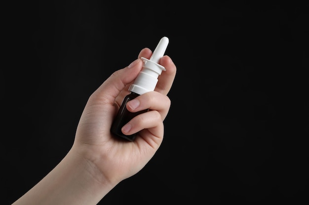 Woman with nasal spray on black background closeup Space for text