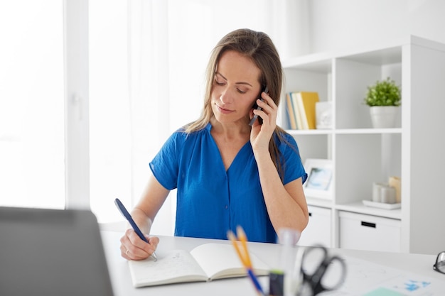 woman with notepad calling on smartphone at office