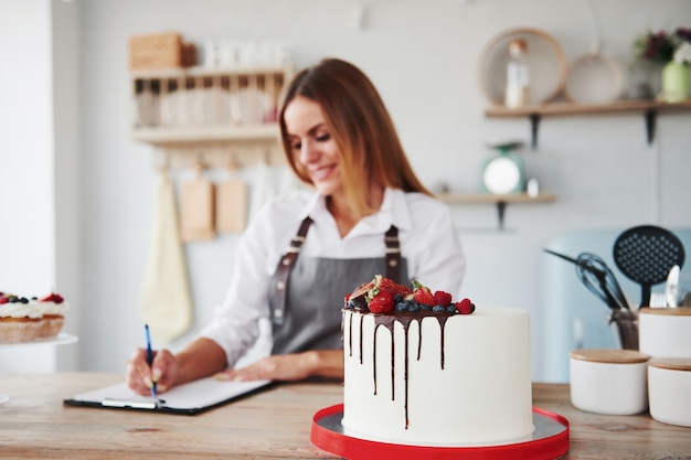 La donna con il blocco note sta all'interno in cucina con i biscotti sul tavolo.