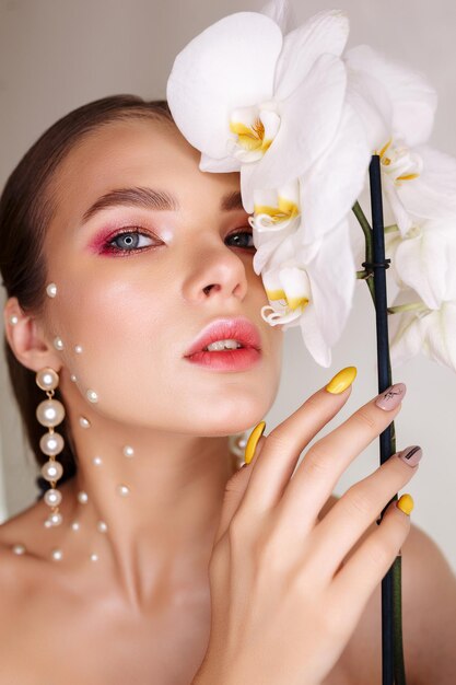 蘭の顔の近くの女性顔に真珠と白い花を持つ女性モデル