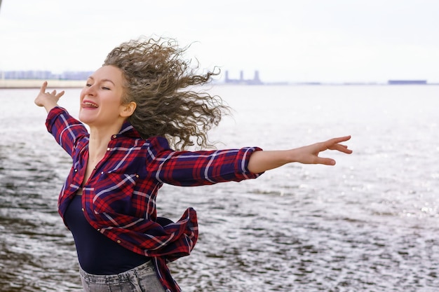 Woman with outstretched arms to the side against the background of water enjoying freedom