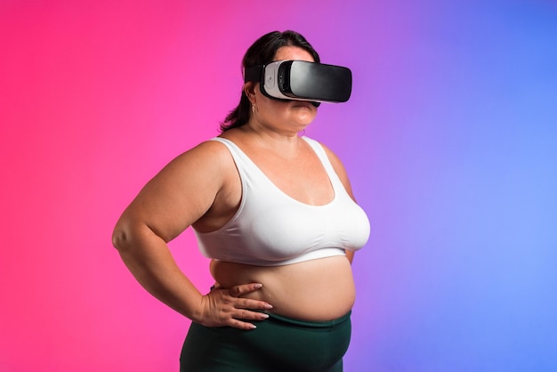 Woman with overweight in a tracksuit and VR headset posing in a studio with blue and red background