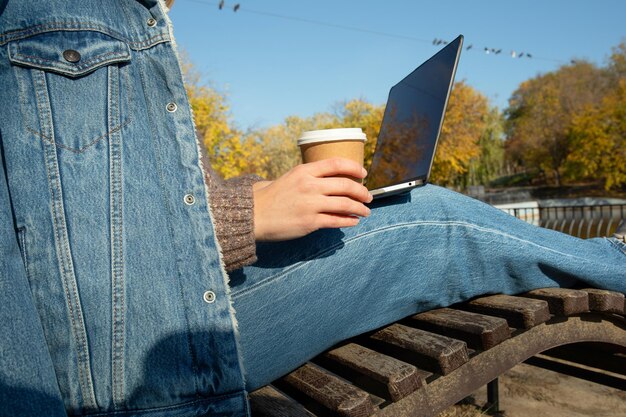 Woman with paper cup and laptop in park