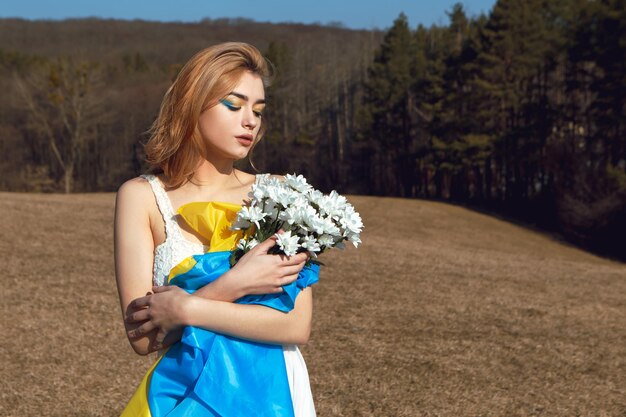 Woman with patriotic makeup wrapped in ukrainian flag Stand with Ukraine concept