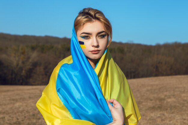 Женщина с патриотическим макияжем, завернутая в украинский флаг, стоит с концепцией Украины