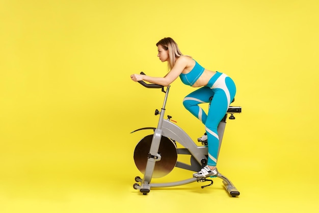 Foto donna con un corpo perfetto che guida la cyclette a casa facendo uno sforzo per perdere qualche chilo in più