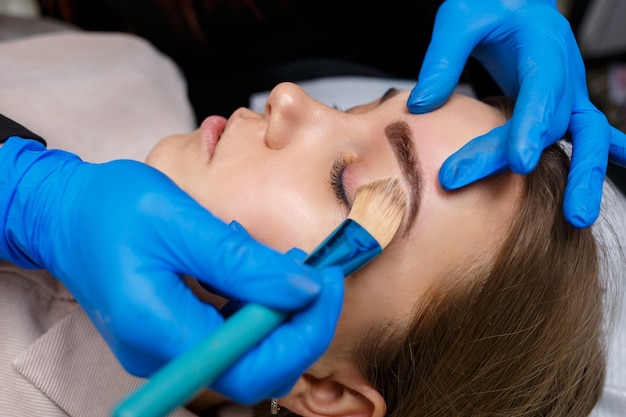 Woman with permanent makeup tattoo on her eyebrows. Close-up beautician makes makeup applies a foundation. Professional make-up and cosmetic skin care.