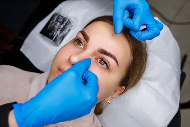 Woman with permanent makeup tattoo on her eyebrows. Close-up beautician makes a sketch of the eyebrows. Professional make-up and cosmetic skin care.