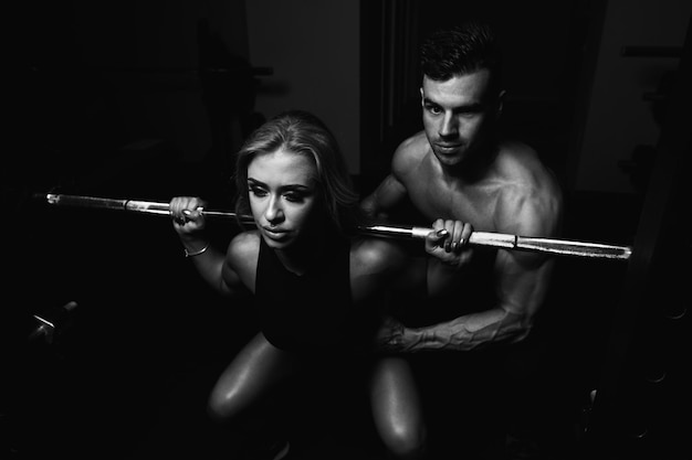 Woman With Personal Trainer At Barbell Squat