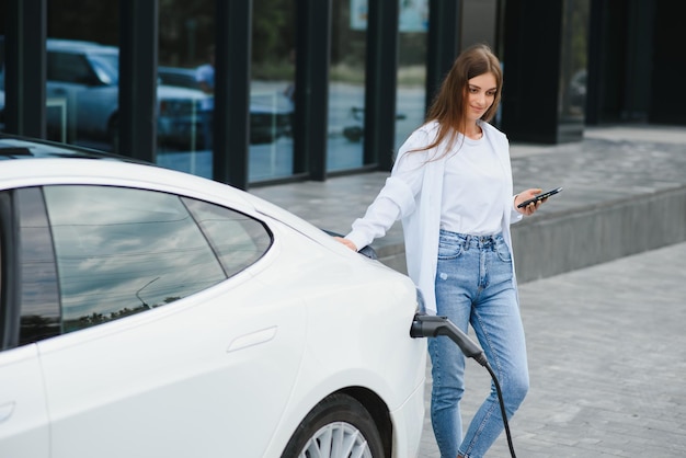 Woman with phone near an rental electric car Vehicle charged at the charging station