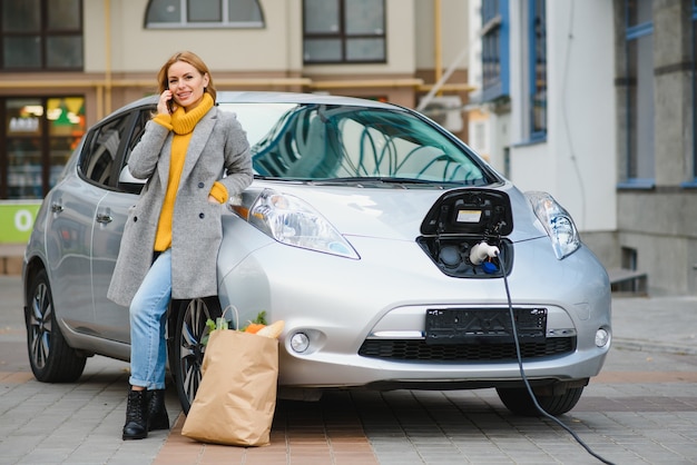 レンタル電気自動車の近くに電話を持つ女性