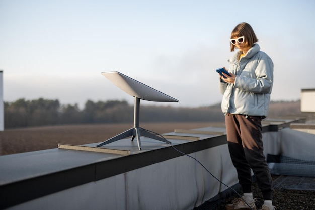 電話を持つ女性は、屋根の上でスターリンク衛星インターネットを使用しています