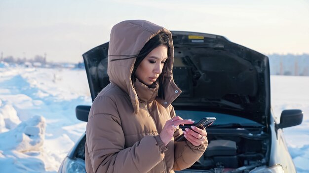 Woman with phone waits for tow truck near broken car