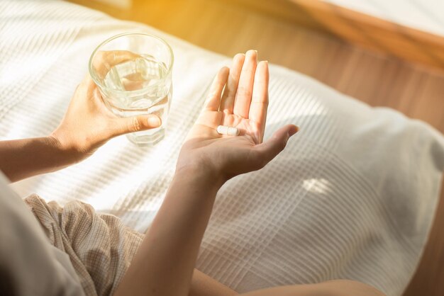 Woman with pills or capsules on hand and a glass of water