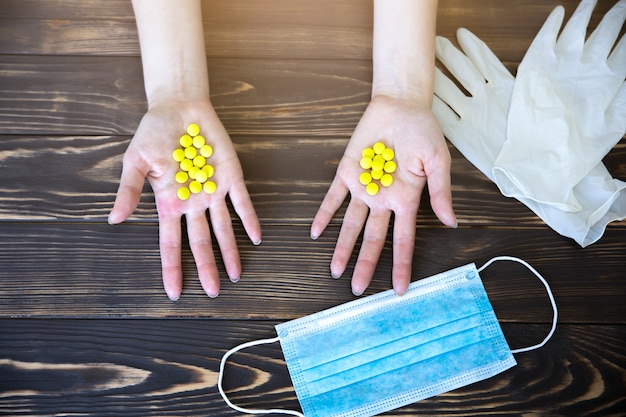 Woman with pills in hands. Medical mask and rubber gloves on background. Virus illness. Coronavirus pandemia danger. Flu and cold in winter.