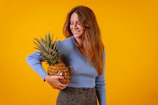 Woman with a pineapple in sunglasses portrait with pineapple in hand studio on yellow background