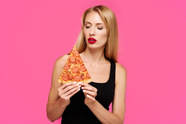 분홍색 배경을 가진 여성이 손에 피자를 들고 건강에 해로운 지방 정크 푸드의 개념