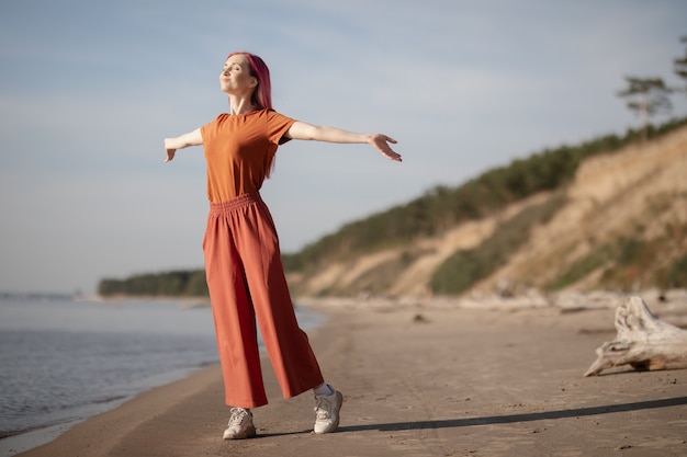 woman with pink hair enjoying the sun and wind on the beach