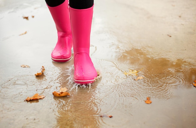 Woman with pink rubber boots walking through puddle in autumn