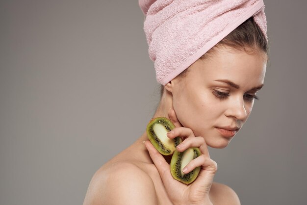 Woman with pink towel on her head bare shoulders cropped view of kiwi fruit in health hand