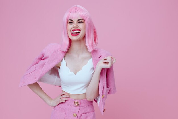 A woman with a pink wig and pink hair is posing on a pink background