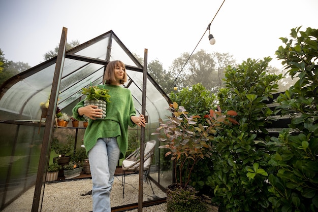 裏庭の温室の近くに植物を持つ女性