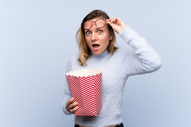 Woman with popcorns over isolated blue wall 