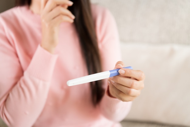 Woman with pregnancy test positive result, focus on foreground 2 stripes.