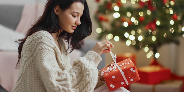 Женщина с подарком в подарочной коробке возле елки дома